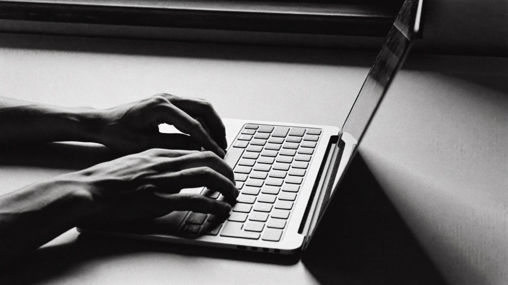 ノートパソコンのキーボードに置かれた両手（白黒写真）