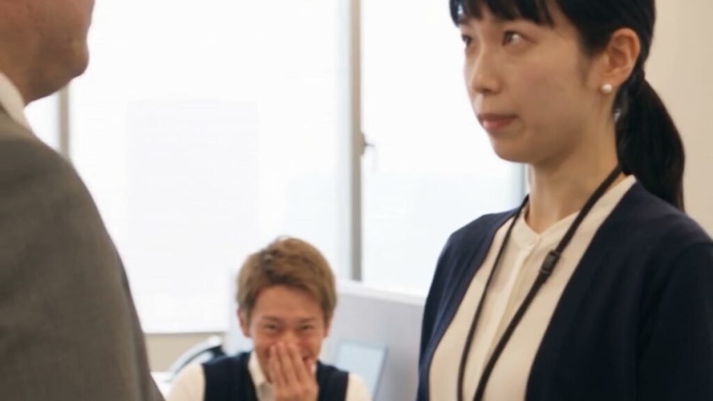 『派遣監査人』の一場面。部長の前に立つ佐倉と、後ろで口を押さえて笑う同僚の高梨